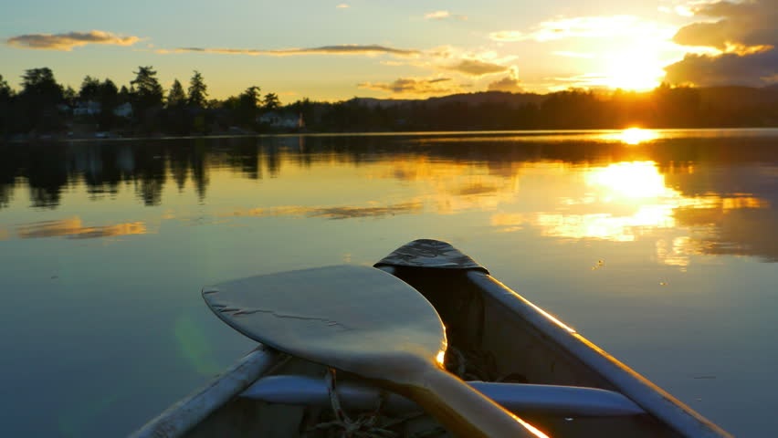 Image of canoe front and paddle with lake, trees and sunrise in background