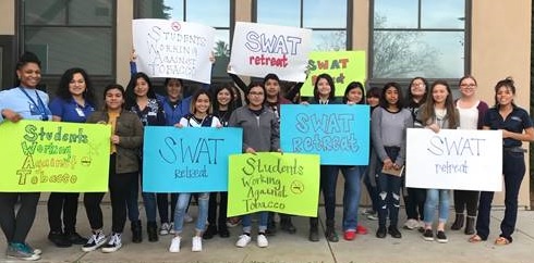 Group of teenagers and Public Health Staff, holding signs saying SWAT"Students Working against Tobacco" outside of a building