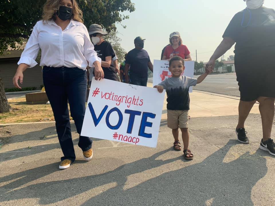 Woman and child holding a sign. Sign states: #voting rights, VOTE, #naacp