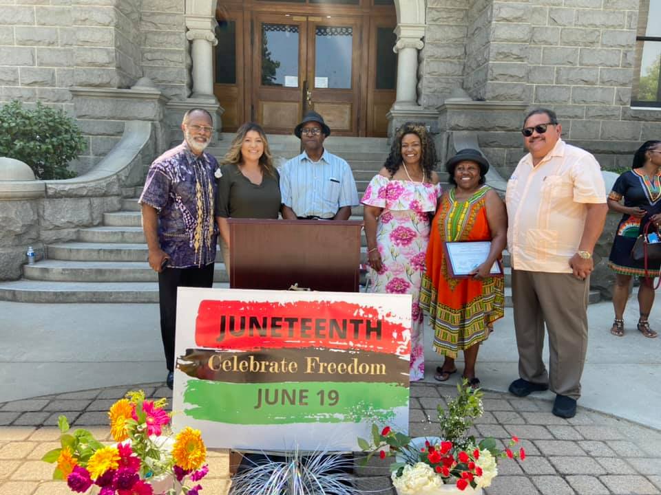 people gathered in front of a podium with a red,black, and green sign that states Juneteenth celebrate freedom June 19 